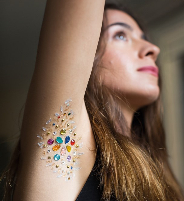 Des perles et paillettes sont collées sur l’aisselle d’une femme qui lève le bras.