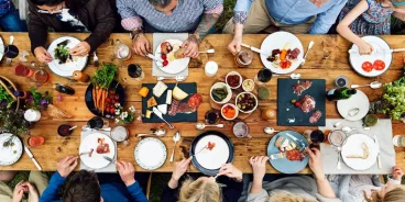 Un groupe de convives attablés autour d’une table en bois garnie de produits culinaires