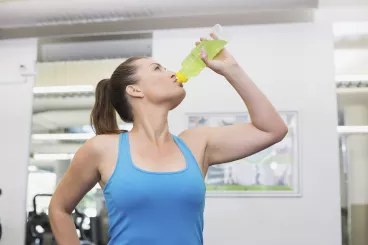 Que boire avant, pendant et après l'effort ? Femme sportive en train de boire pendant sa séance d’exercice pour s'hydrater