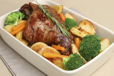 Gigot d’agneau servi à table dans son plat et ses légumes