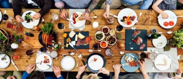 Un groupe de convives attablés autour d’une table en bois garnie de produits culinaires