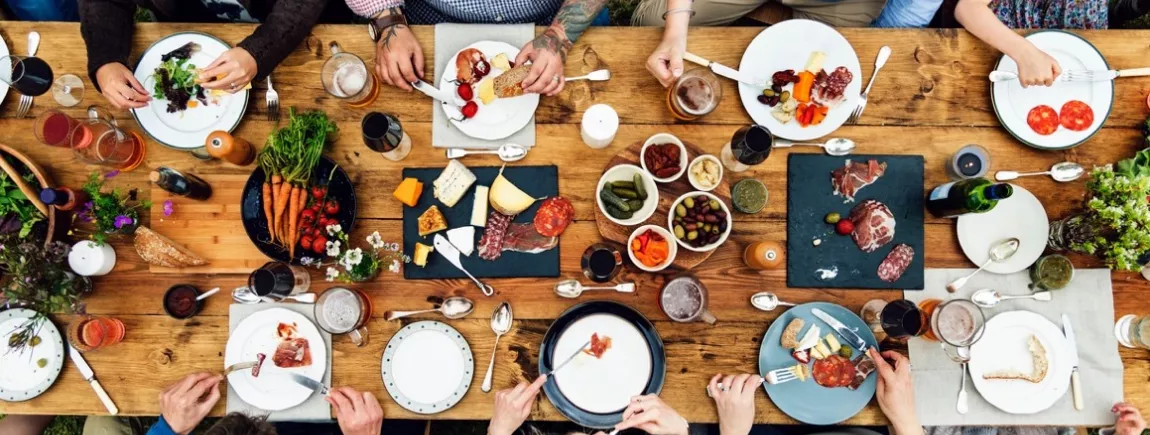 Un groupe de convives attablés autour d’une table en bois garnie de produits culinaires