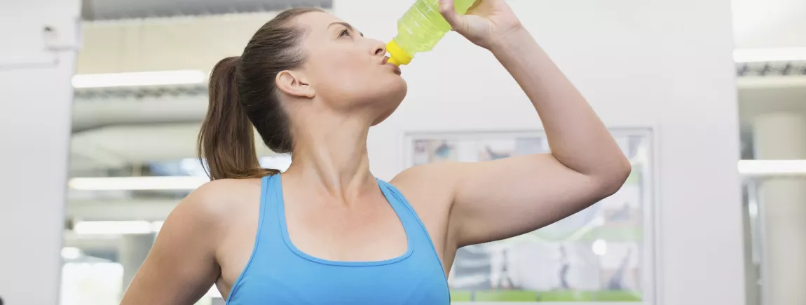 Que boire avant, pendant et après l'effort ? Femme sportive en train de boire pendant sa séance d’exercice pour s'hydrater